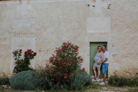 Femme enceinte et son compagnon appuyés contre une porte devant leur maison gersoise
